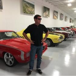 Photo of Ken Thwaits standing in front of his car collection